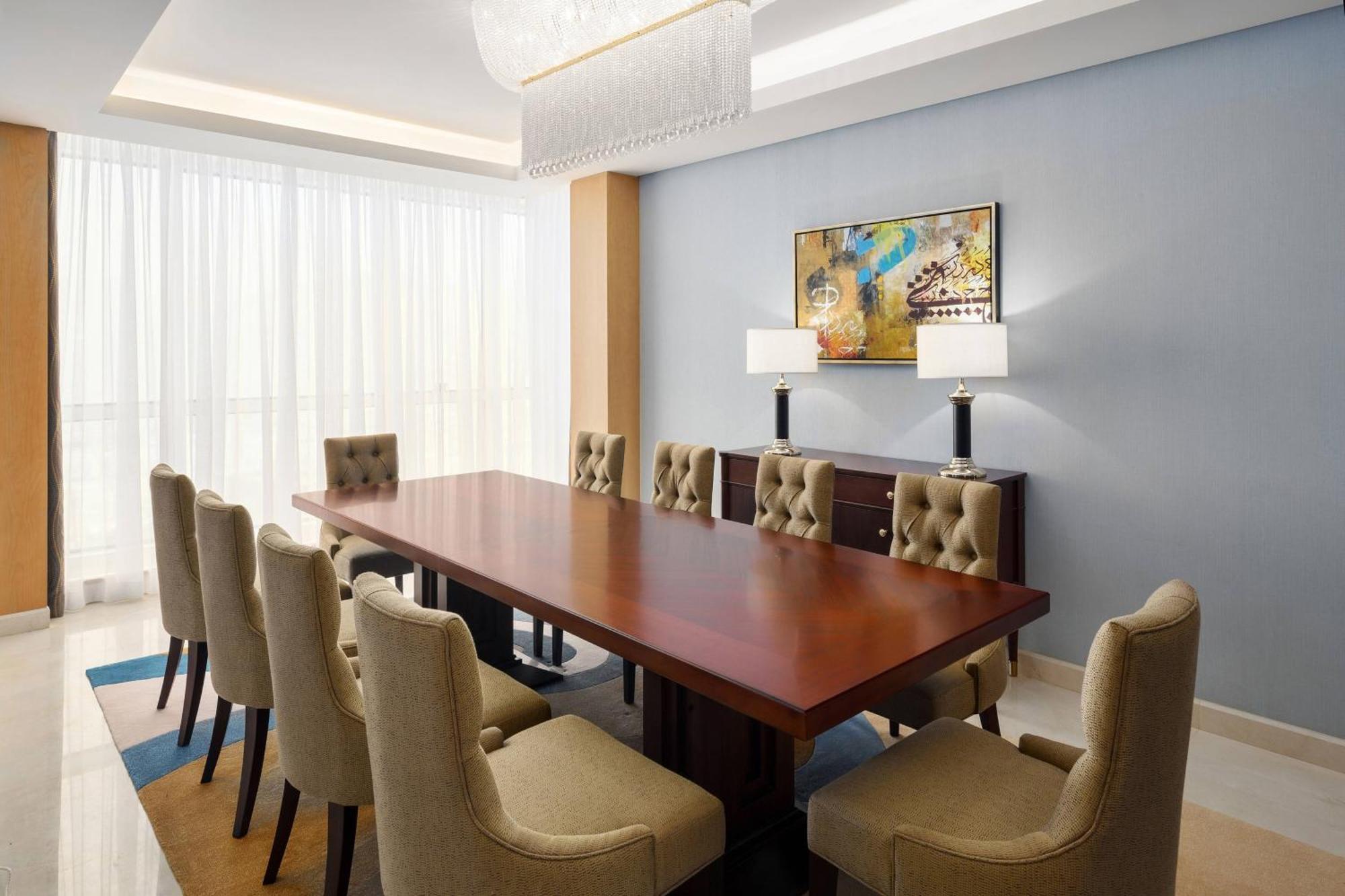 Sheraton Makkah Jabal Al Kaaba Hotel La Meca Exterior foto The photo shows a spacious and elegantly designed conference room. It features a large wooden conference table surrounded by upholstered chairs. The chairs have a beige color and a tufted design. On one side of the room, there are two contemporary la