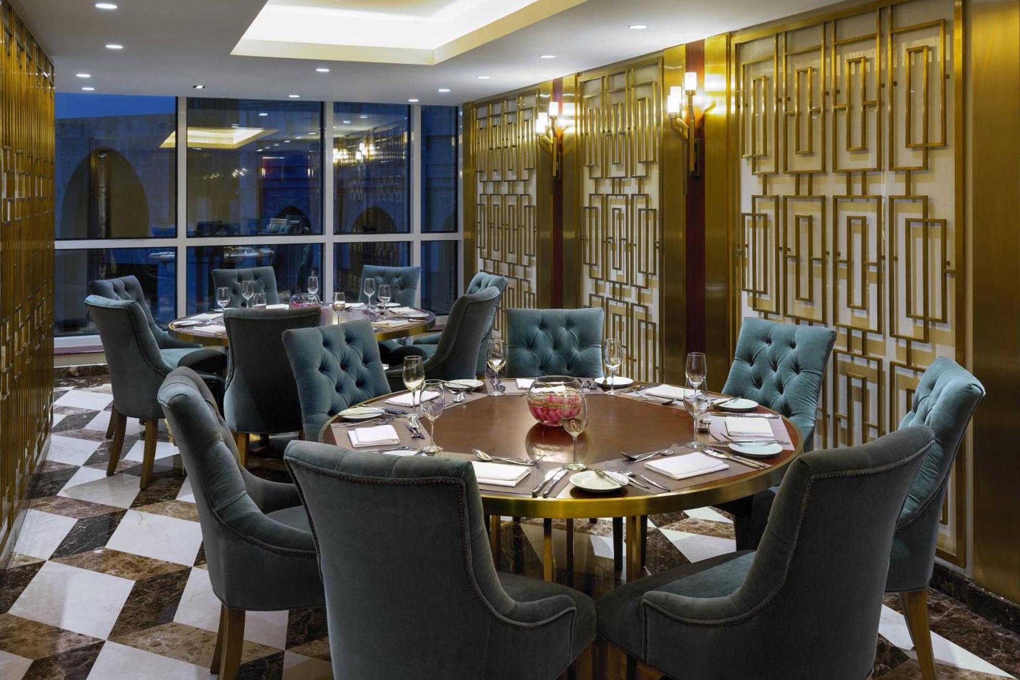 Sheraton Makkah Jabal Al Kaaba Hotel La Meca Exterior foto The photo shows an elegant dining room with a sophisticated ambiance. It features a round wooden table at the center, surrounded by plush chairs upholstered in a soft, teal fabric. The room has a stylish décor, highlighted by a geometrically patterne