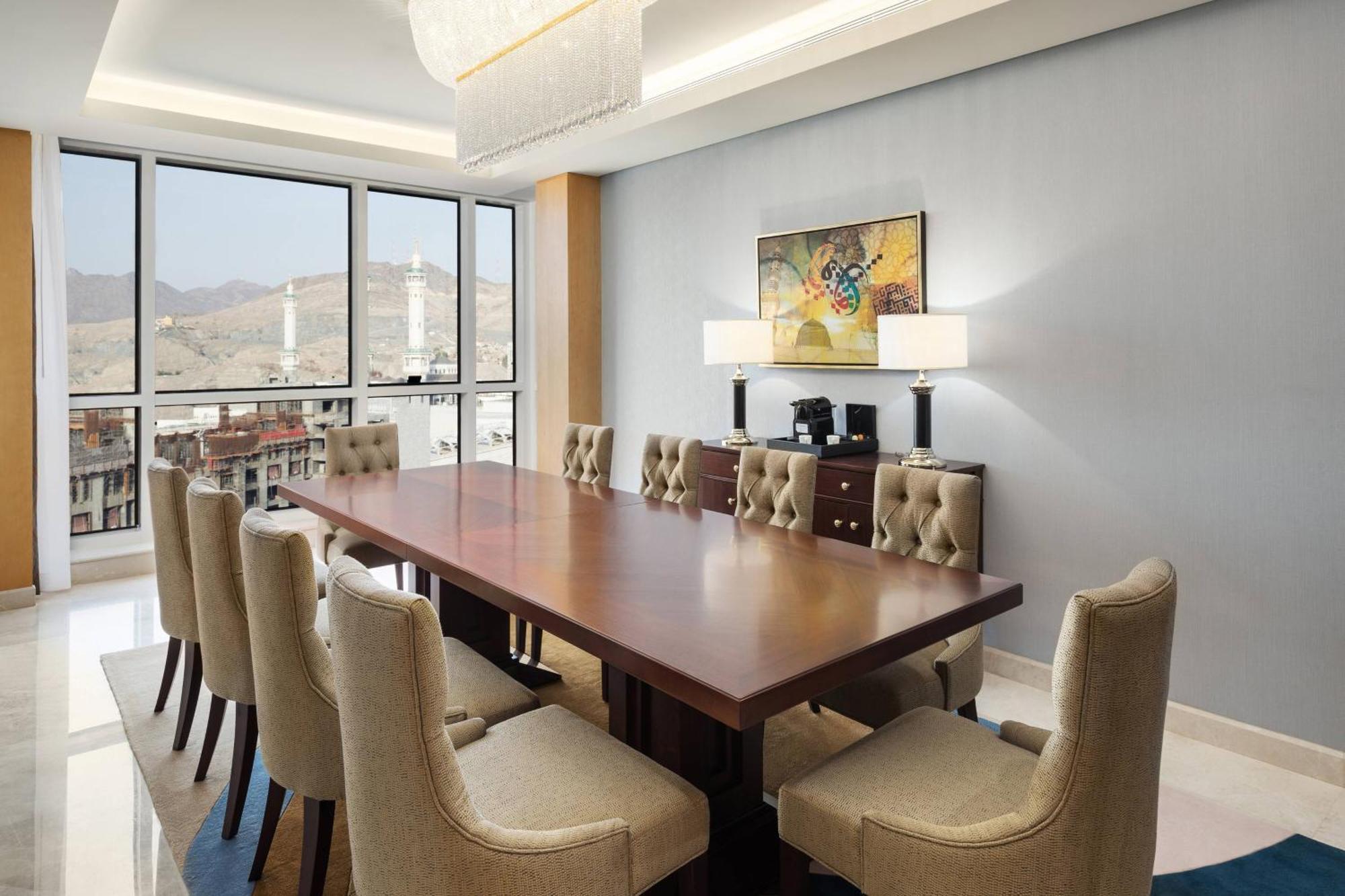 Sheraton Makkah Jabal Al Kaaba Hotel La Meca Exterior foto The photo shows a modern conference room with a large wooden table surrounded by upholstered chairs. The room is well-lit, featuring large windows that offer a view of the outdoors, possibly with mountains in the background. On one wall, there is a p