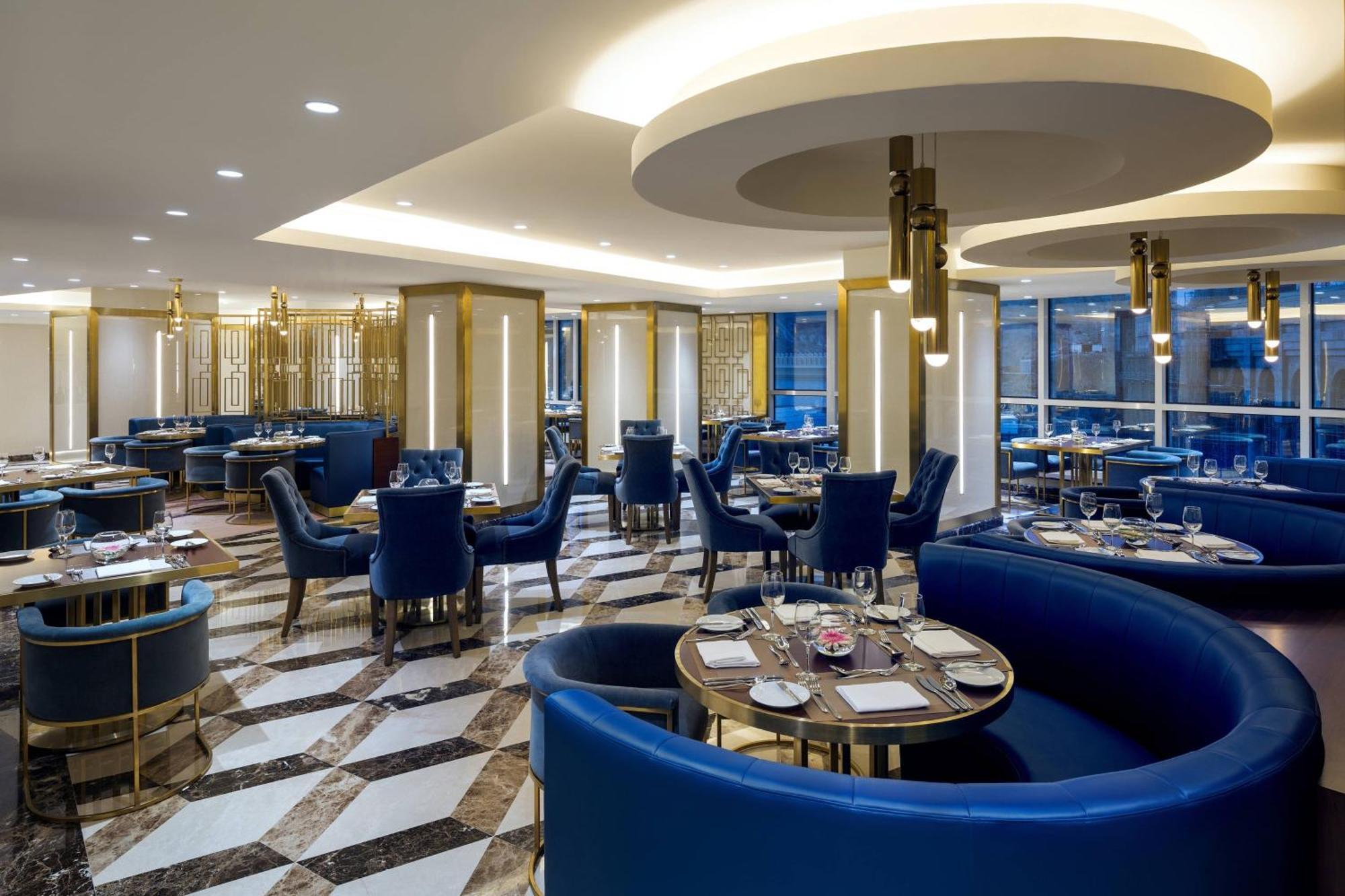 Sheraton Makkah Jabal Al Kaaba Hotel La Meca Exterior foto The photo shows the interior of a modern restaurant. The design features elegant curved blue seating arranged around round tables with plates and glassware set for dining. The flooring is a striking marble pattern, adding to the upscale ambiance. The